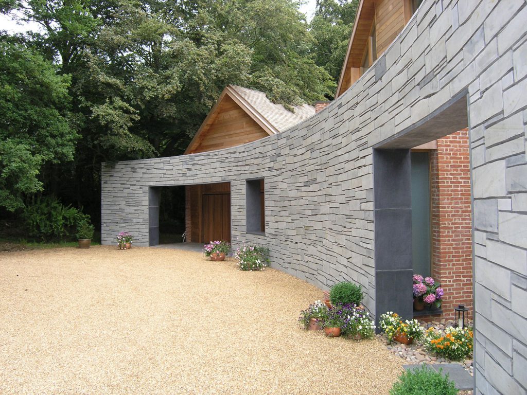 The design and construction of a new private house set within the green belt. The house sits within a mature garden, surrounded by trees to the North, with open views to the South. The materials reflect the rural nature of the site. Cedar shingles and screens form the roof and end walls, whilst the entrance drive is lined by a curved slate wall.